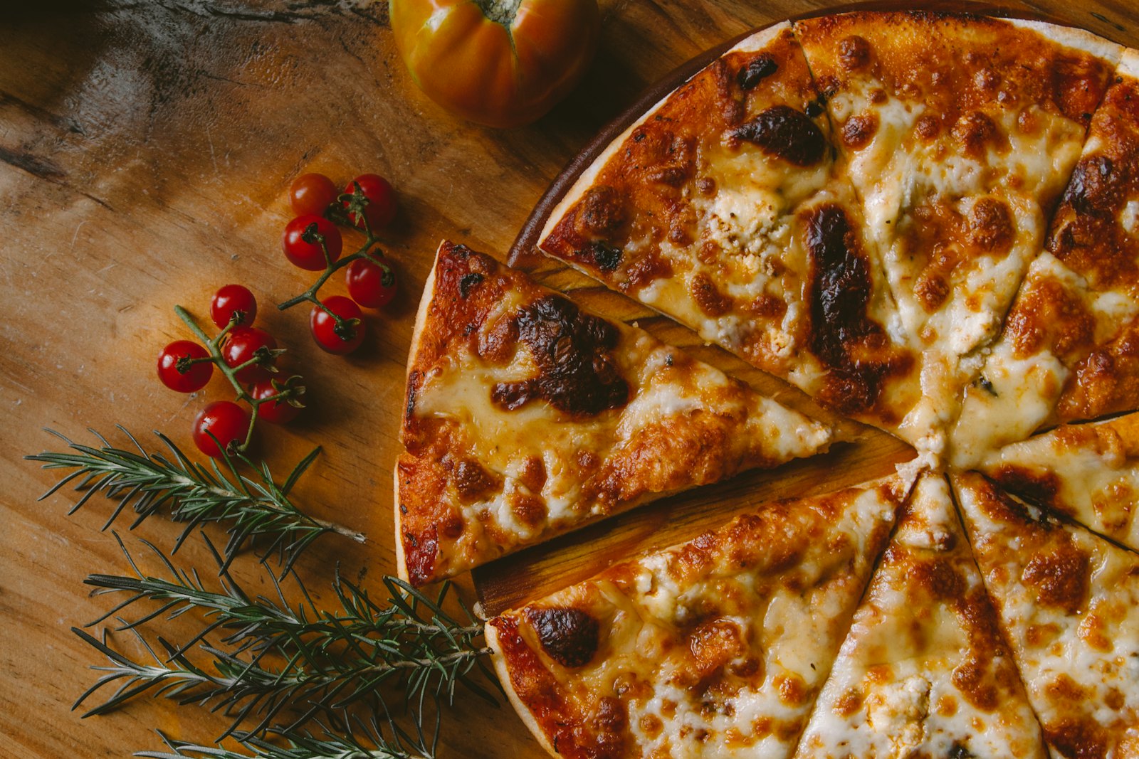 Pizza fatiada em tábua de madeira com tomates-cereja e alecrim