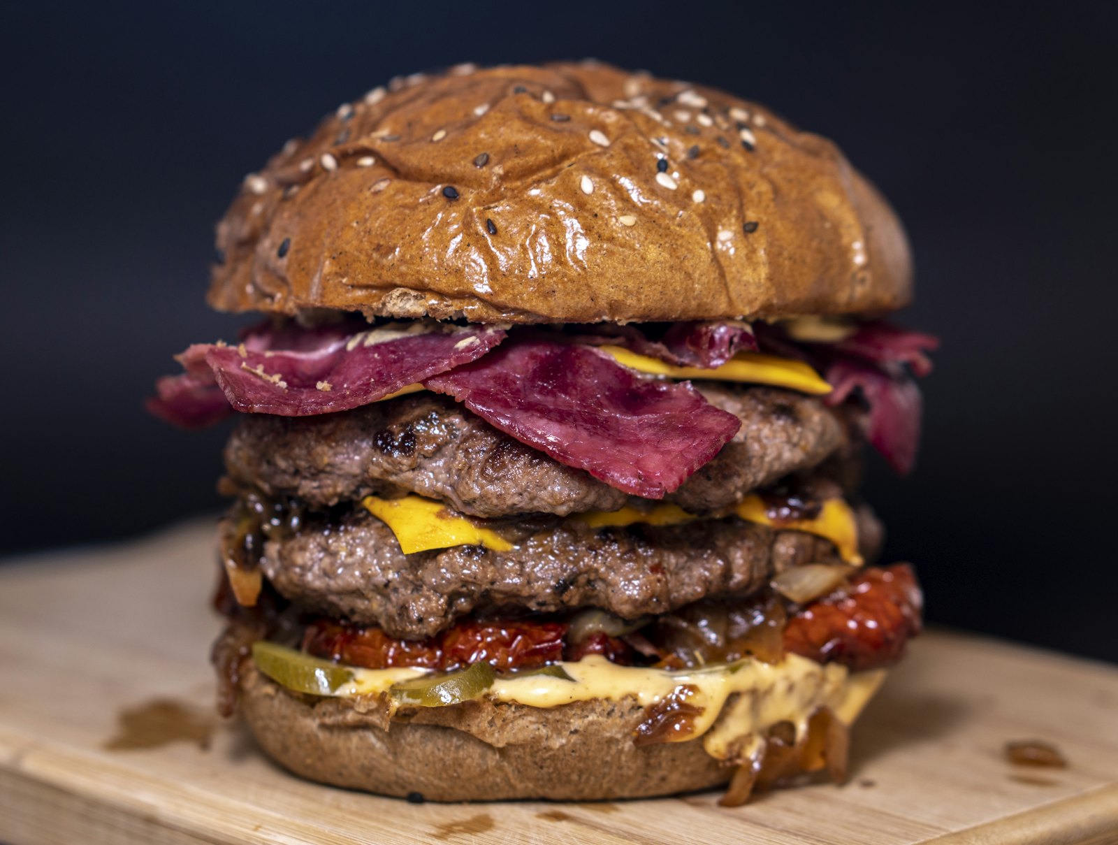 Lanche alto com duas carnes, queijo e bacon, em fundo escuro